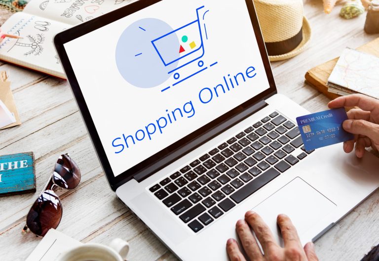 Compuradora con imagen de un carrito de e-commerce y una tarjeta de crédito en la mano