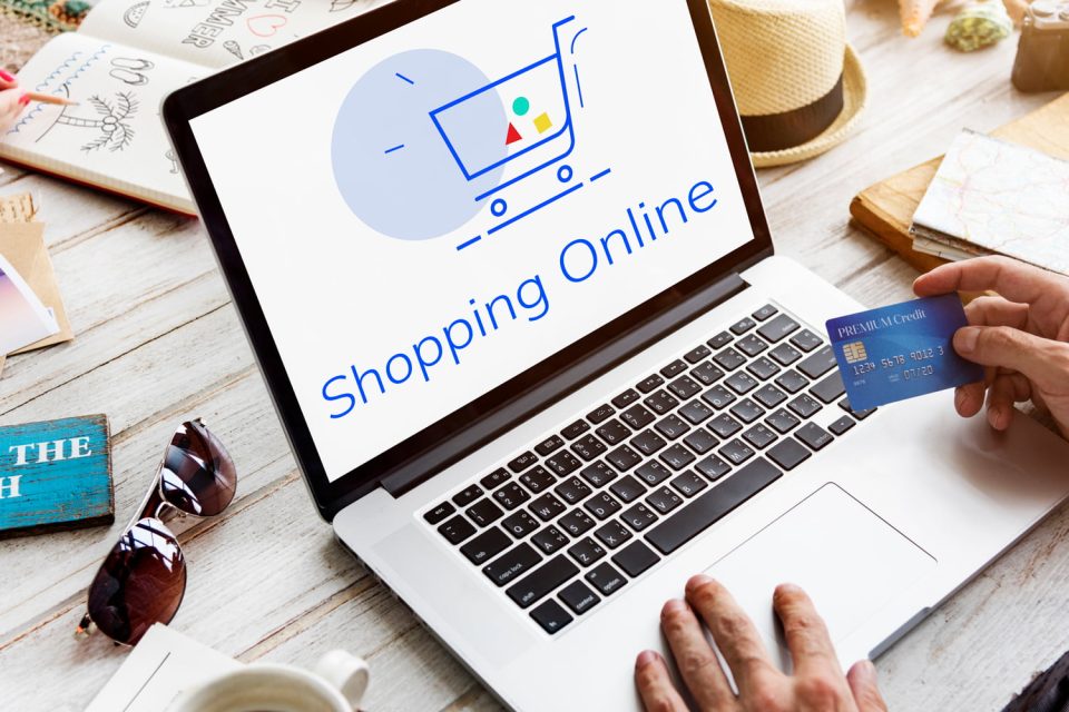 Compuradora con imagen de un carrito de e-commerce y una tarjeta de crédito en la mano